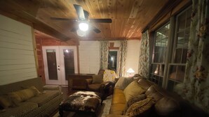 A cozy living room with a wooden ceiling, a brown leather sofa, patterned cushions, and a small table with a lamp.