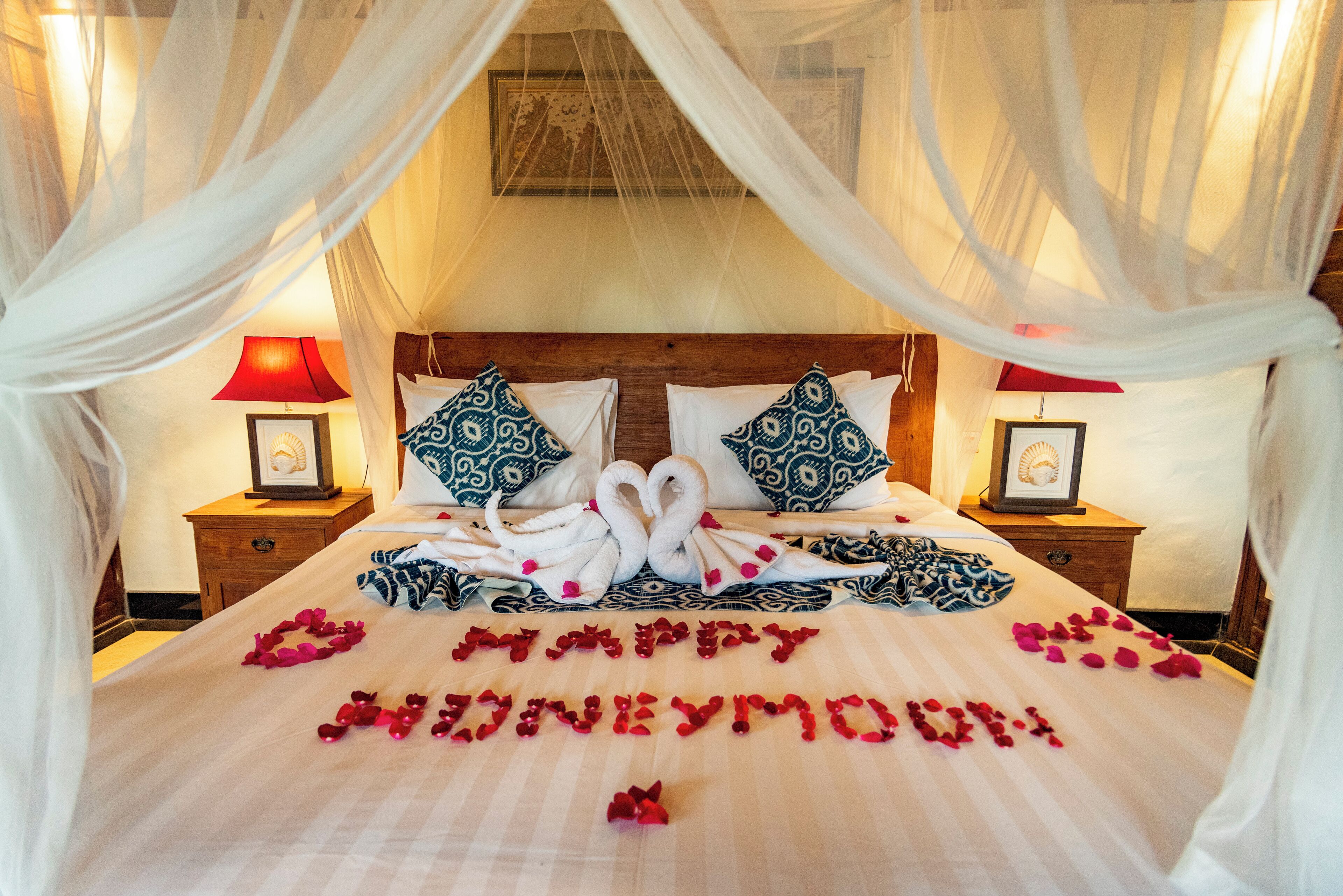 A bed with a canopy, two pillows, a bedside table with a lamp, and a framed picture on the wall.