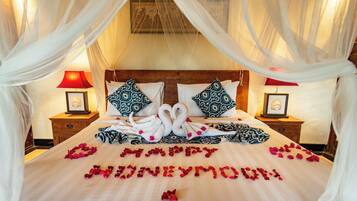 A bed with a canopy, two pillows, a bedside table with a lamp, and a framed picture on the wall.
