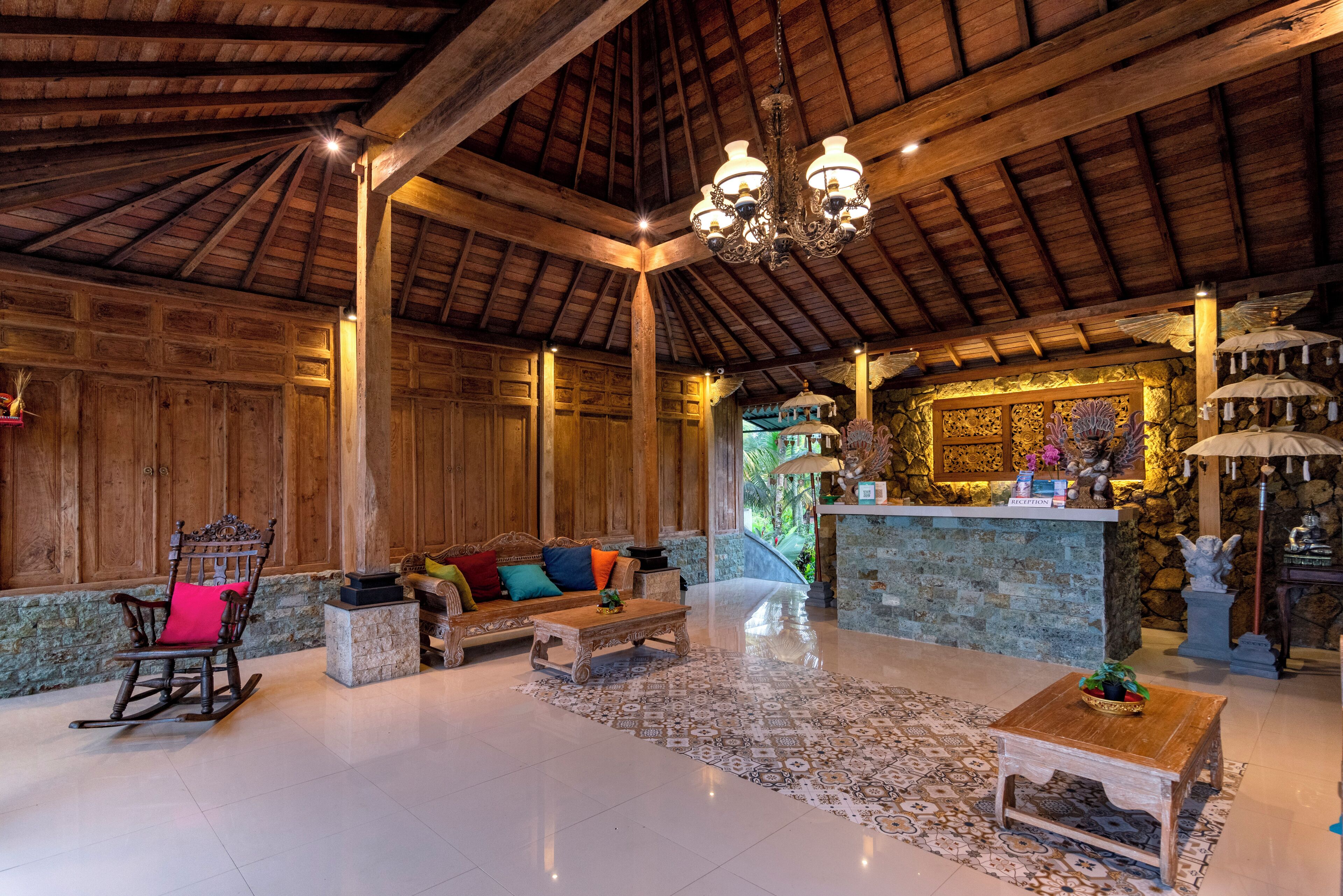 Un vestíbulo espacioso con un alto techo de madera, un candelabro, un mostrador de recepción y una zona de estar con un sofá y un sillón mecedora.