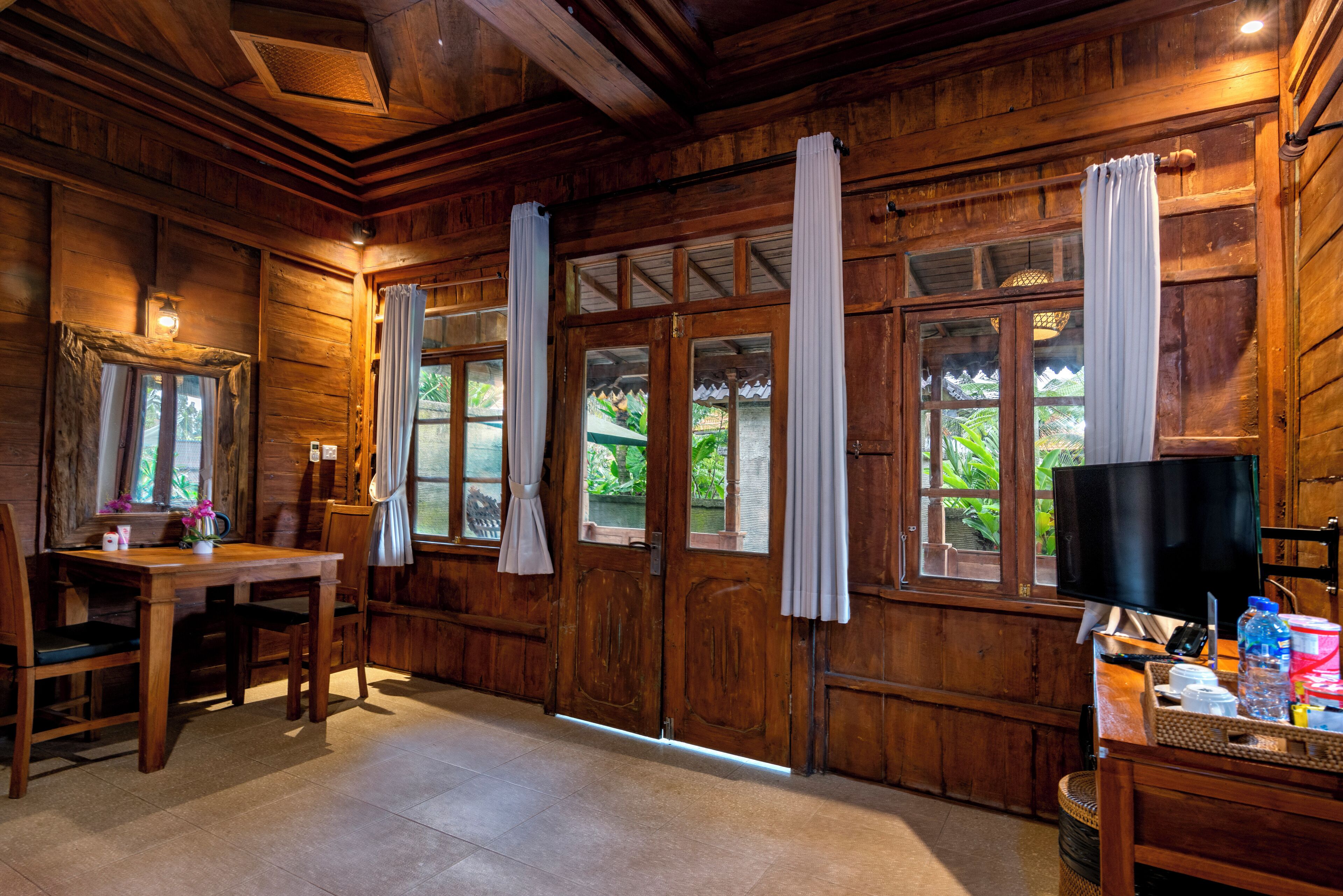 A wooden interior with a dining table, chairs, a television, and curtains on large windows.