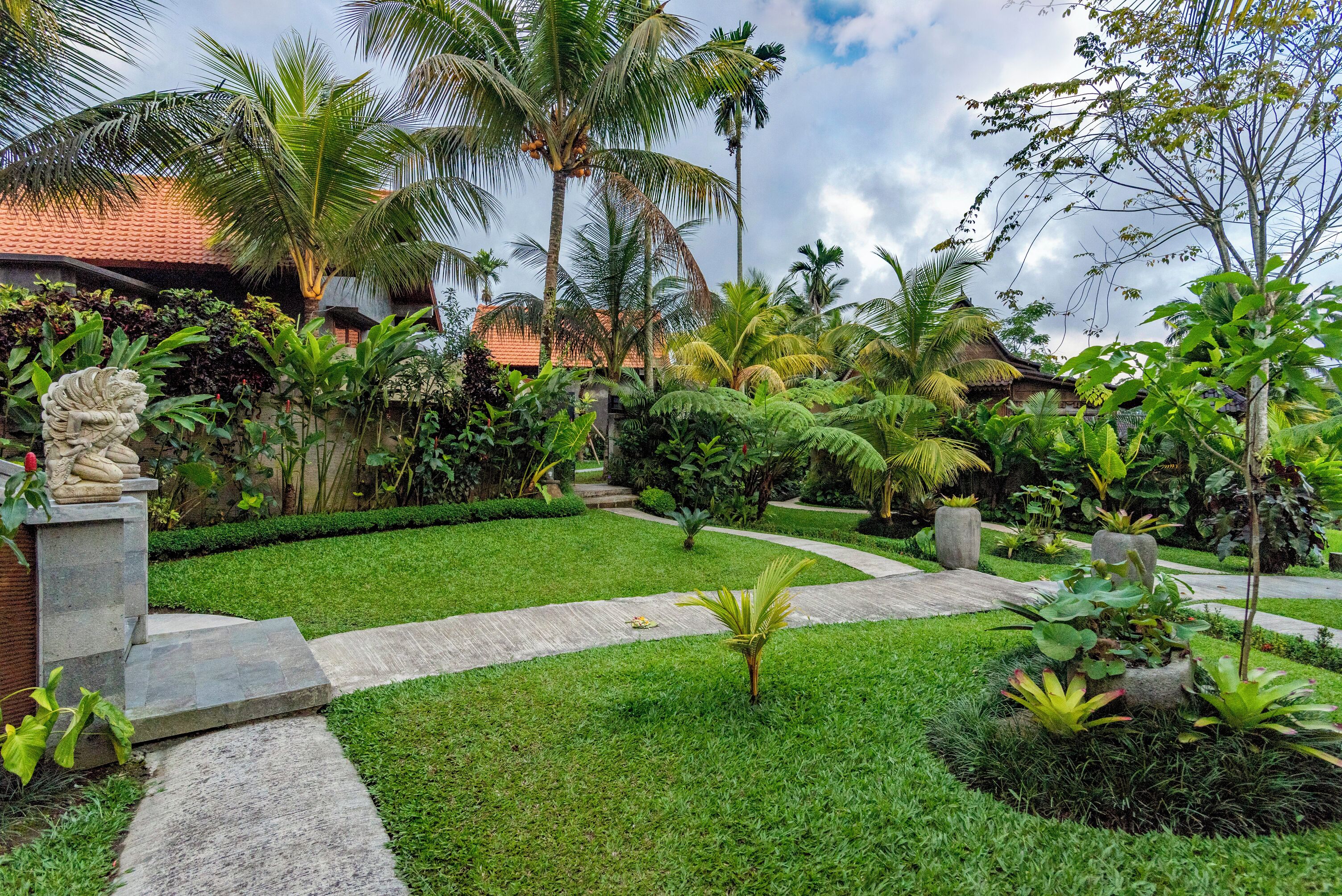 Un jardin tropical avec un sentier, des palmiers et une maison en briques.