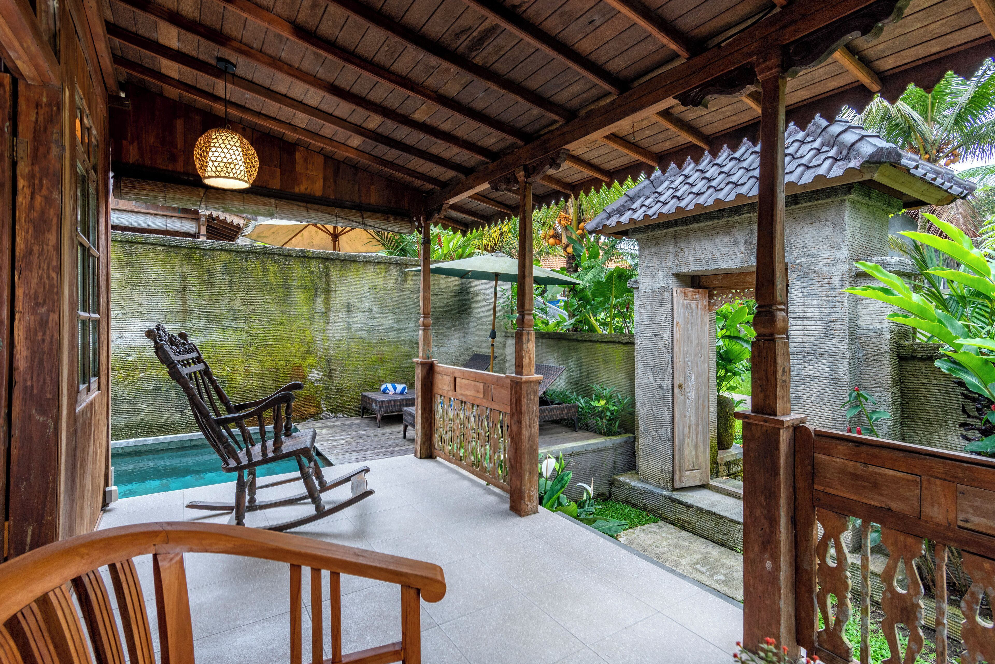 A wooden deck with a swing chair and a table, a small pool, and a stone building with a tiled roof.