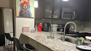 Una cocina moderna con encimera de granito, electrodomésticos de acero inoxidable y taburetes negros.