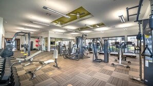 Un gimnasio espacioso con diversos equipos de ejercicio, amplias ventanas y piso de madera.