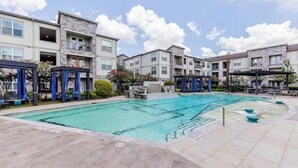 Zona de piscina con caída de agua, rodeada de edificios de varios pisos con balcones.