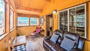 A cozy cabin interior with a wooden ceiling, a leather sofa, a red chair, and a dining table. - Steps to trails • Fireplace • Pet & kid friendly (Big Bear)