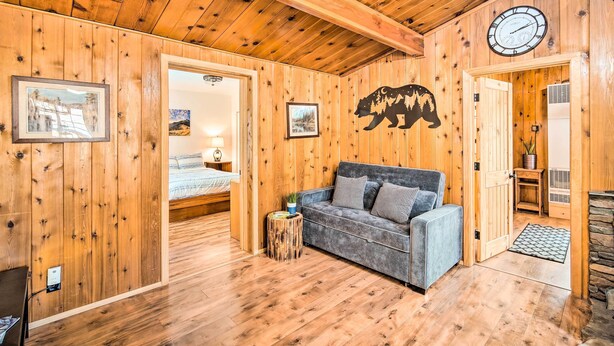 A cozy wooden cabin interior with a sofa, framed pictures, and a bear silhouette on the wall. - Steps to trails • Fireplace • Pet & kid friendly (Big Bear)