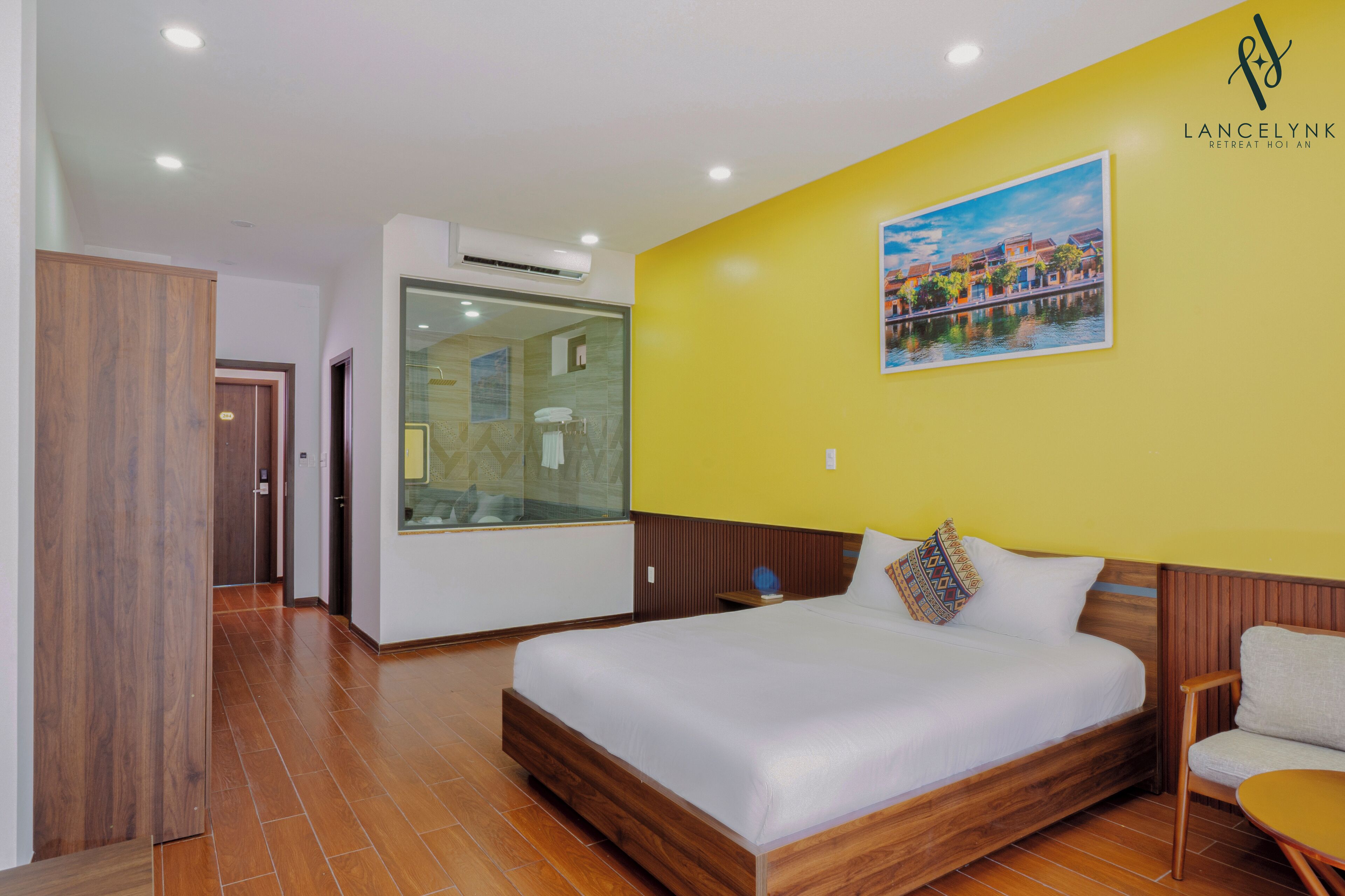 Una habitación de hotel con una cama de madera, cabina de ducha de vidrio y una pared amarilla con un cuadro.