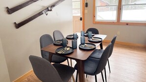 Een eethoek met een houten tafel, zes stoelen en ski's aan de wand.