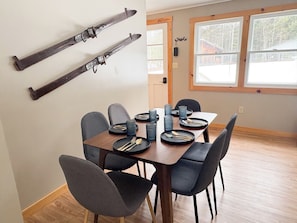 A dining area with a wooden table, six chairs, and skis mounted on the wall.