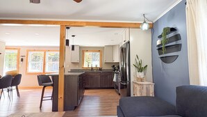 Een moderne woonkamer met een grijze bank, een houten eettafel en een keuken met donkere kasten en een roestvrijstalen koelkast.