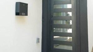 Un ingresso moderno con una porta di colore scuro caratterizzata da listelli orizzontali, una cassetta postale con il numero 1523 e una piccola casetta delle lettere a parete.