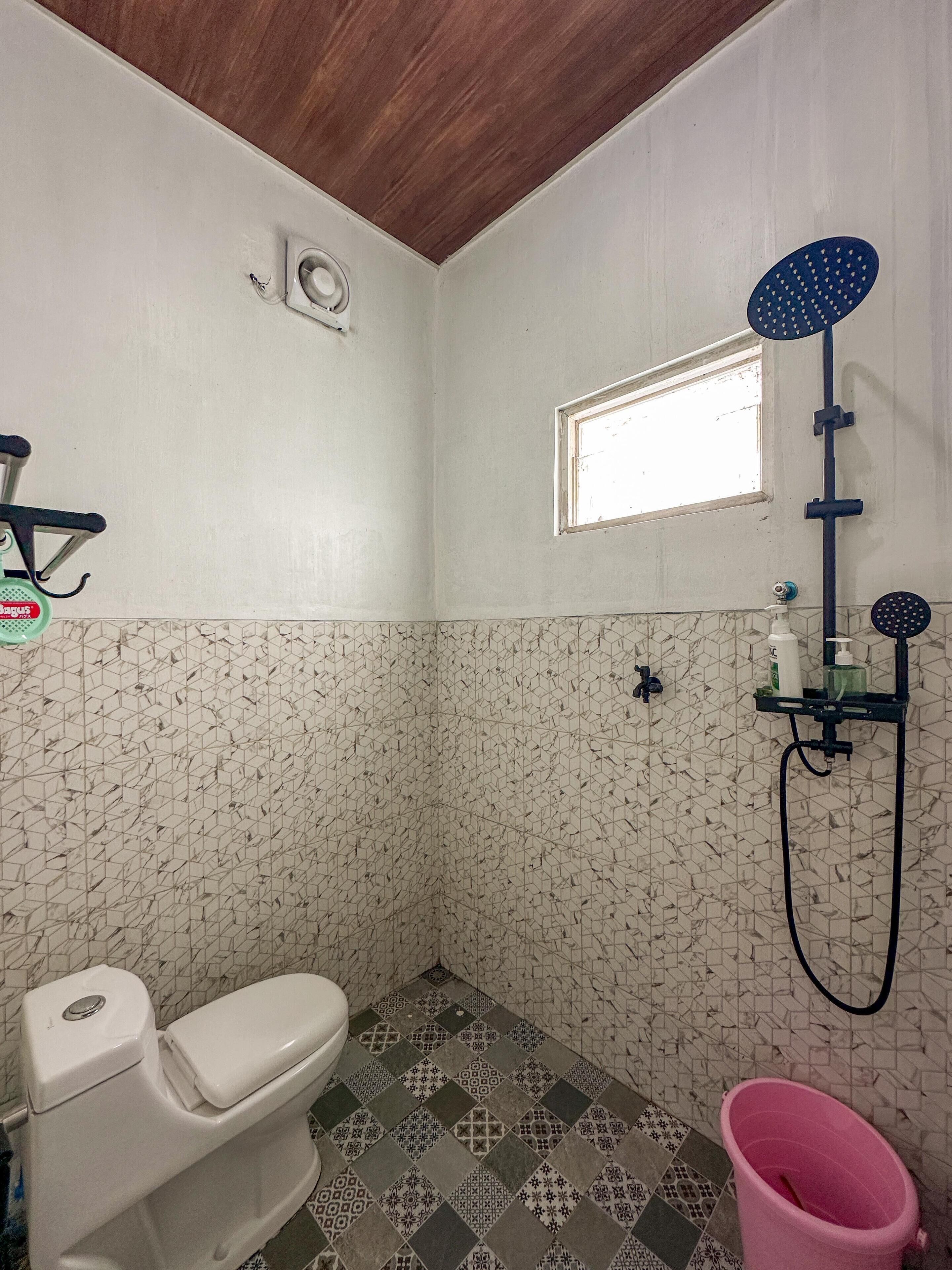 A small bathroom with a toilet, a shower, and a window.