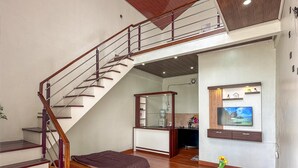 A spacious living area with a wooden staircase, a sofa set, a coffee table, and a television mounted on the wall. - Skypiea dieng (Dieng Kulon)
