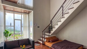 A spacious living area with a wooden floor, a sofa, a coffee table, and a view through large windows. - Skypiea dieng (Dieng Kulon)