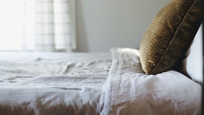 Ein Bett mit weißer Bettwäsche und einem braunen Kopfkissen.