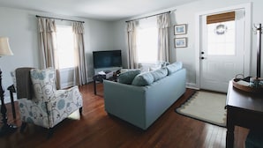 Ein Wohnzimmer mit Sofa, Sessel, Fernseher und einer Tür mit einem Kranz.