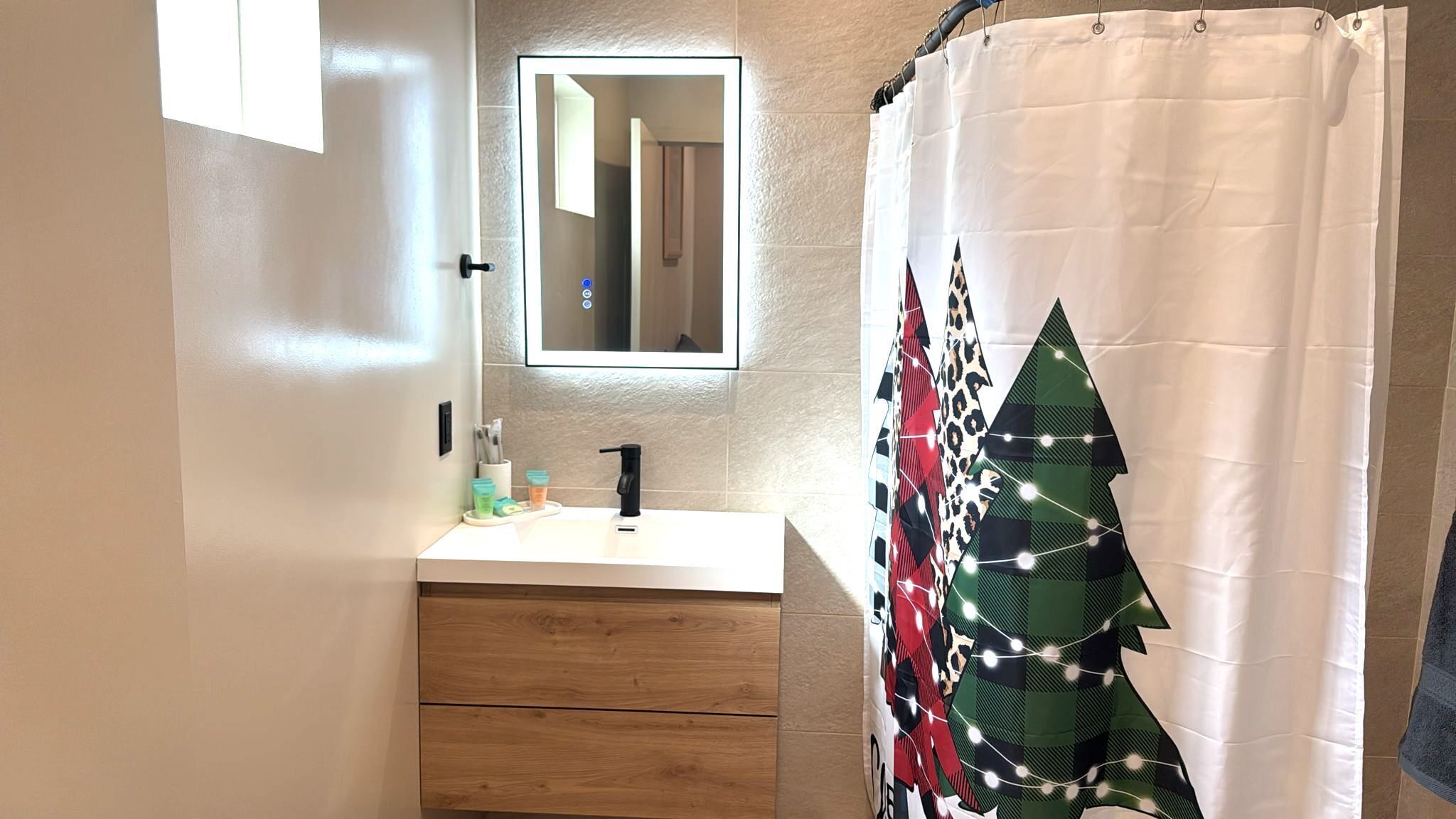 A bathroom with a white sink, a mirror above it, and a shower curtain with a Christmas tree design.
