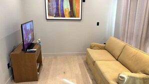 Una sala de estar con un televisor de pantalla plana sobre un soporte de madera, un sofá color beige y un cuadro abstracto y colorido en la pared.
