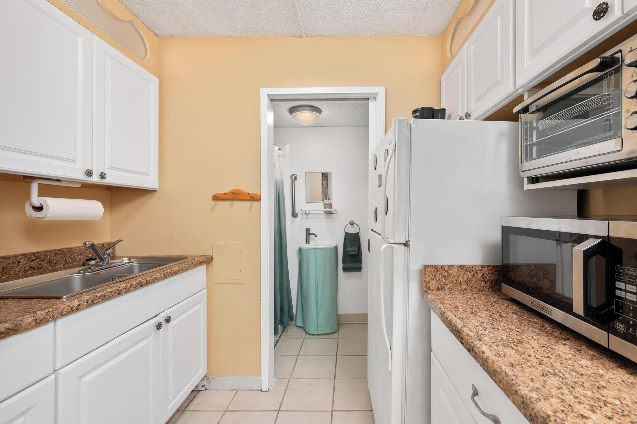 A compact kitchen with white cabinets, a granite countertop, a built-in microwave, and a refrigerator.