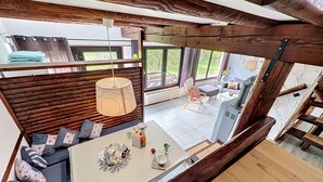 Een modern interieur met een eethoek, een bank met kussens, een hanglamp en uitzicht door grote ramen.