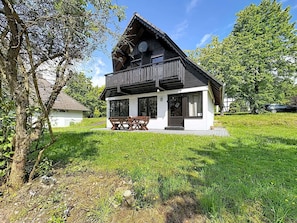A two-story wooden house with a balcony, a dining table and chairs outside, surrounded by greenery. - Lovely apartment in villa for 5 guests with WIFI and patio (Bad Wildungen)
