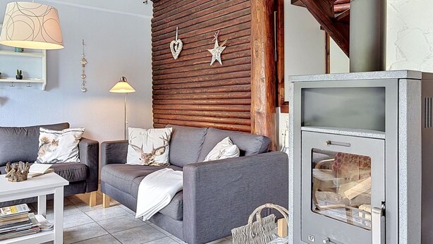 Een knusse woonkamer met een bank, een tafel, een open haard en houten balken.
