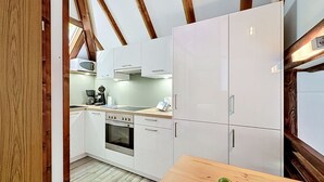 Een moderne keuken met witte kasten, een ingebouwde oven en een houten eettafel met fruit.