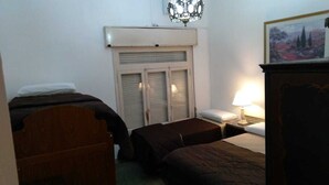 Quarto com duas camas de solteiro, cabeceira de madeira, mesa de cabeceira com abajur e janela com persianas.