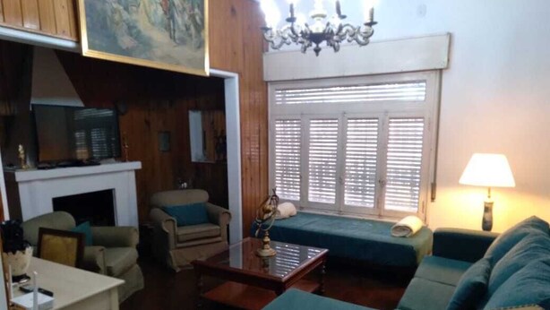 Uma sala de estar com sofá, poltronas, mesa de centro, lareira e uma janela grande com persianas.