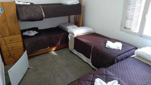 Quarto com beliches, cómoda de madeira e janela com persianas.