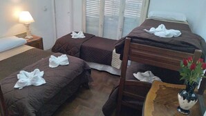 Um quarto com três beliches, uma mesinha de cabeceira com abajur, uma mesa de madeira com um vaso de flores e uma janela com persianas.