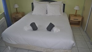 Una cama bien hecha con sábanas blancas, dos almohadas y dos toallas sobre la cama. Hay dos mesitas de noche con lámparas a cada lado de la cama.
