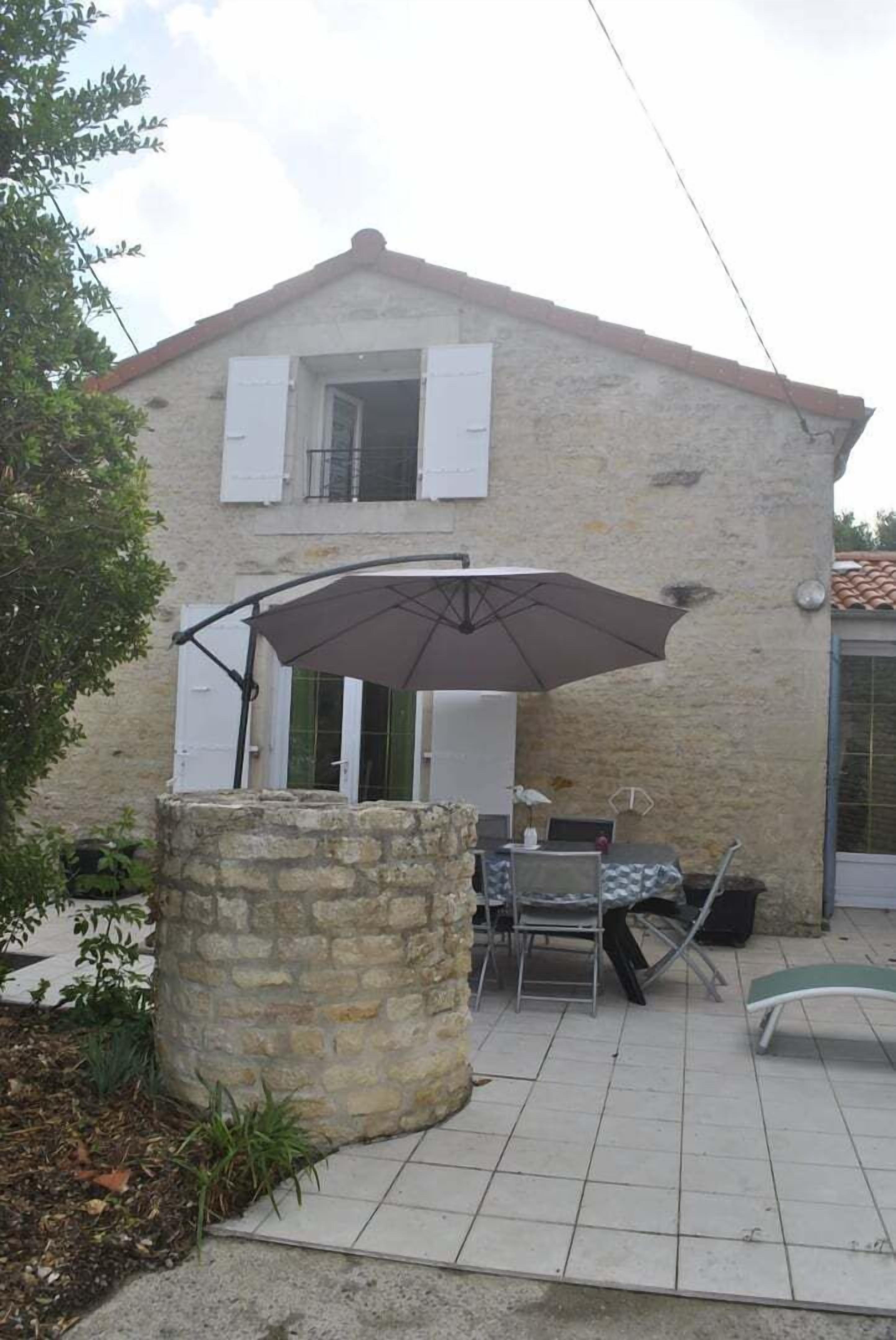 Een stenen huis met een betegeld terras, een tafel met stoelen en een grote parasol.