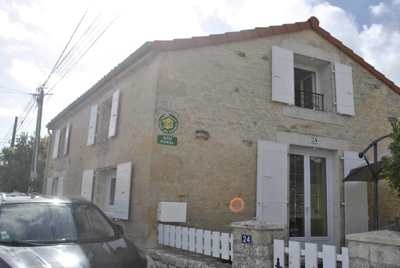 Un edificio de dos plantas con fachada de piedra, un cartel que indica que es una casa rural tipo 'Gîte' y el número 24 en la puerta.