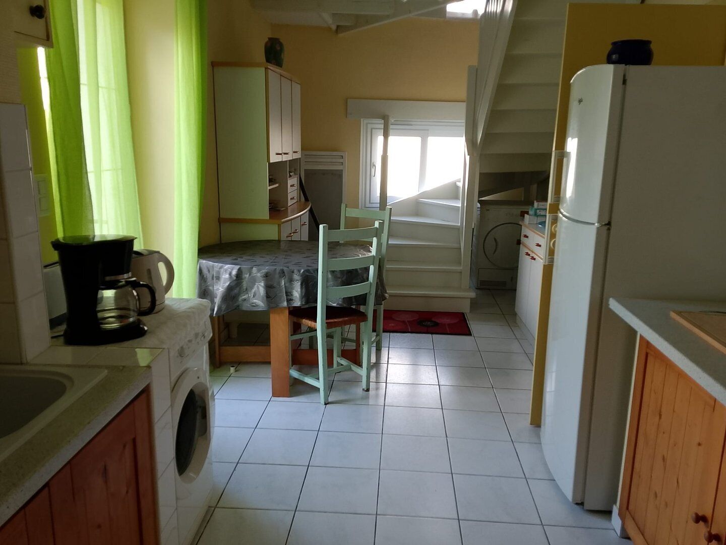 A compact kitchen with a washing machine, a coffee maker, a dining table with chairs, and a refrigerator.