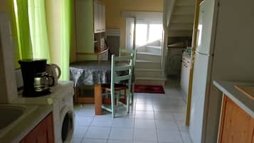 A compact kitchen with a washing machine, a coffee maker, a dining table with chairs, and a refrigerator.