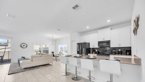 A modern kitchen with white cabinets, a black refrigerator, and a stainless steel microwave. There are three white bar stools and a large island with a sink. - Big house: private pool | Resort | Near Disney (Kissimmee)