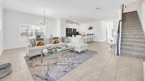 A modern living room with a white sofa, glass coffee table, and a kitchen in the background. - Big house: private pool | Resort | Near Disney (Kissimmee)