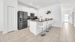 A modern kitchen with white cabinetry, stainless steel appliances, and a central island with bar stools. - Big house: private pool | Resort | Near Disney (Kissimmee)