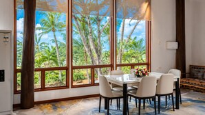 A dining area with a table and chairs, large windows with a tropical view, and a ceiling fan. - Rainbow Holiday Resort (Nadi)