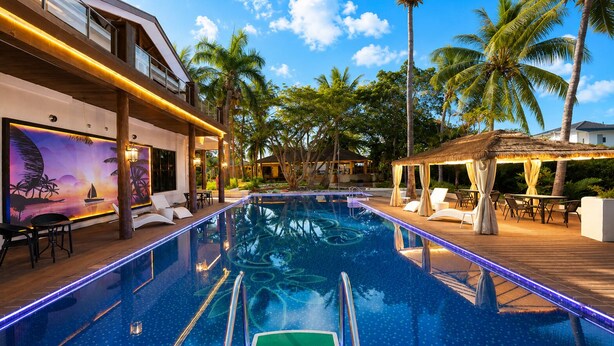 A swimming pool with a wooden deck, lounge chairs, and a sunset mural. - Rainbow Holiday Resort (Nadi)