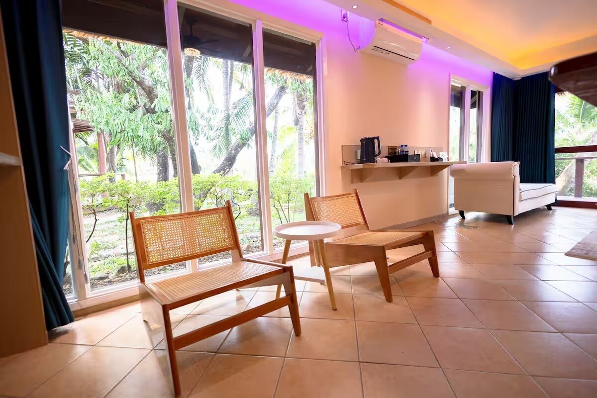 Une pièce avec une grande fenêtre, un canapé blanc, une petite table ronde et une chaise en bois.