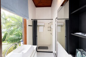 Un baño moderno con bañera, ducha y puertas de cristal que dan a un balcón con vistas a palmeras.