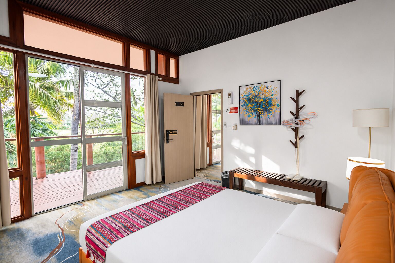 Een hotelkamer met een groot bed, een bankje, een bureau, een stoel, een lamp en een schilderij aan de muur.