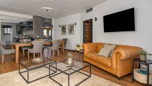 Ein modernes Wohnzimmer mit einer Ledersofa, einem Glastisch und einem Essbereich mit Stühlen und einem Tisch.