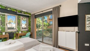 Ein Hotelzimmer mit zwei Betten, einem Schreibtisch, einem Stuhl, einem Fernseher und einer Schiebeglastür zum Balkon.