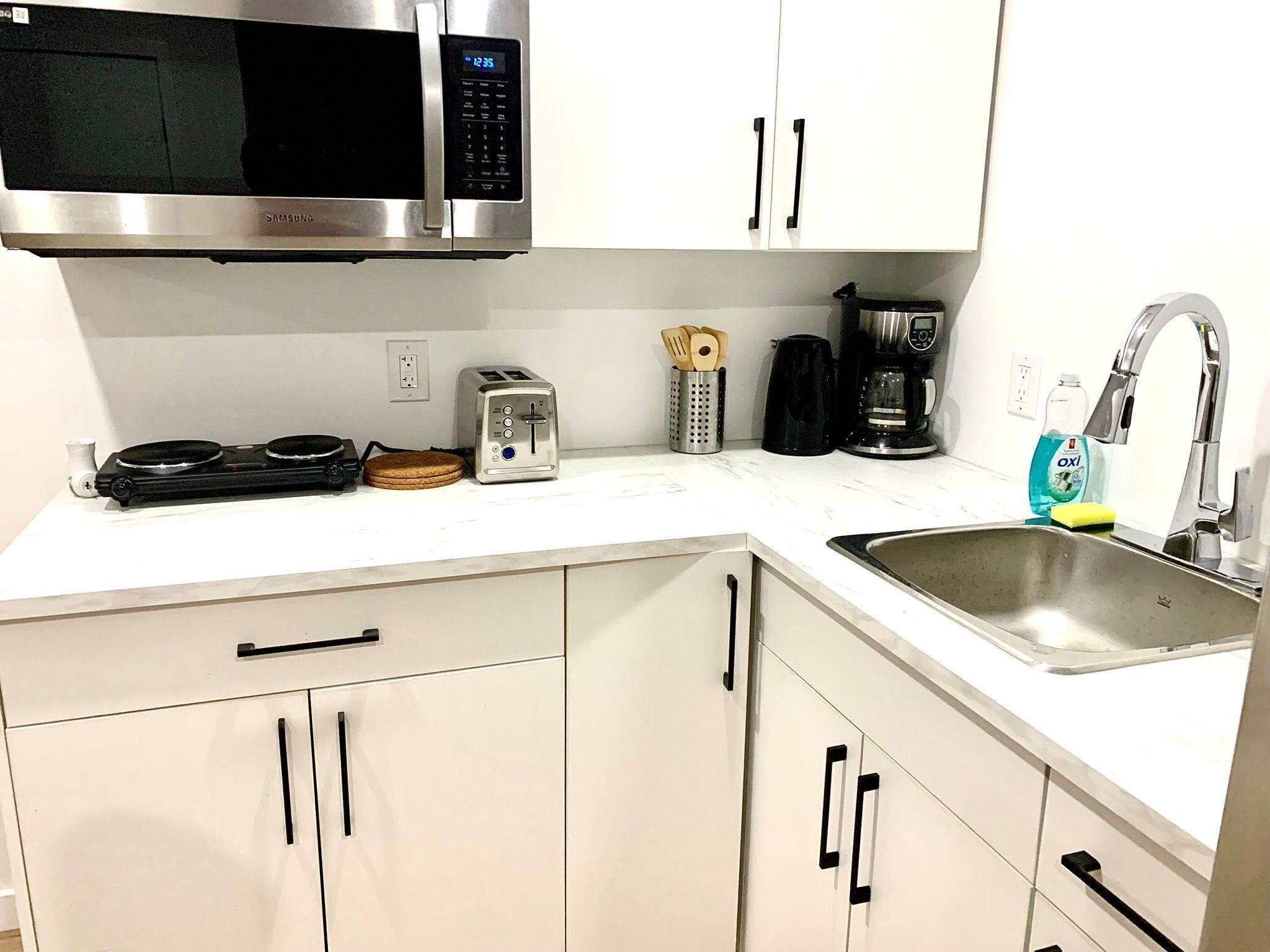A modern kitchen with a microwave, toaster, coffee maker, and a sink.