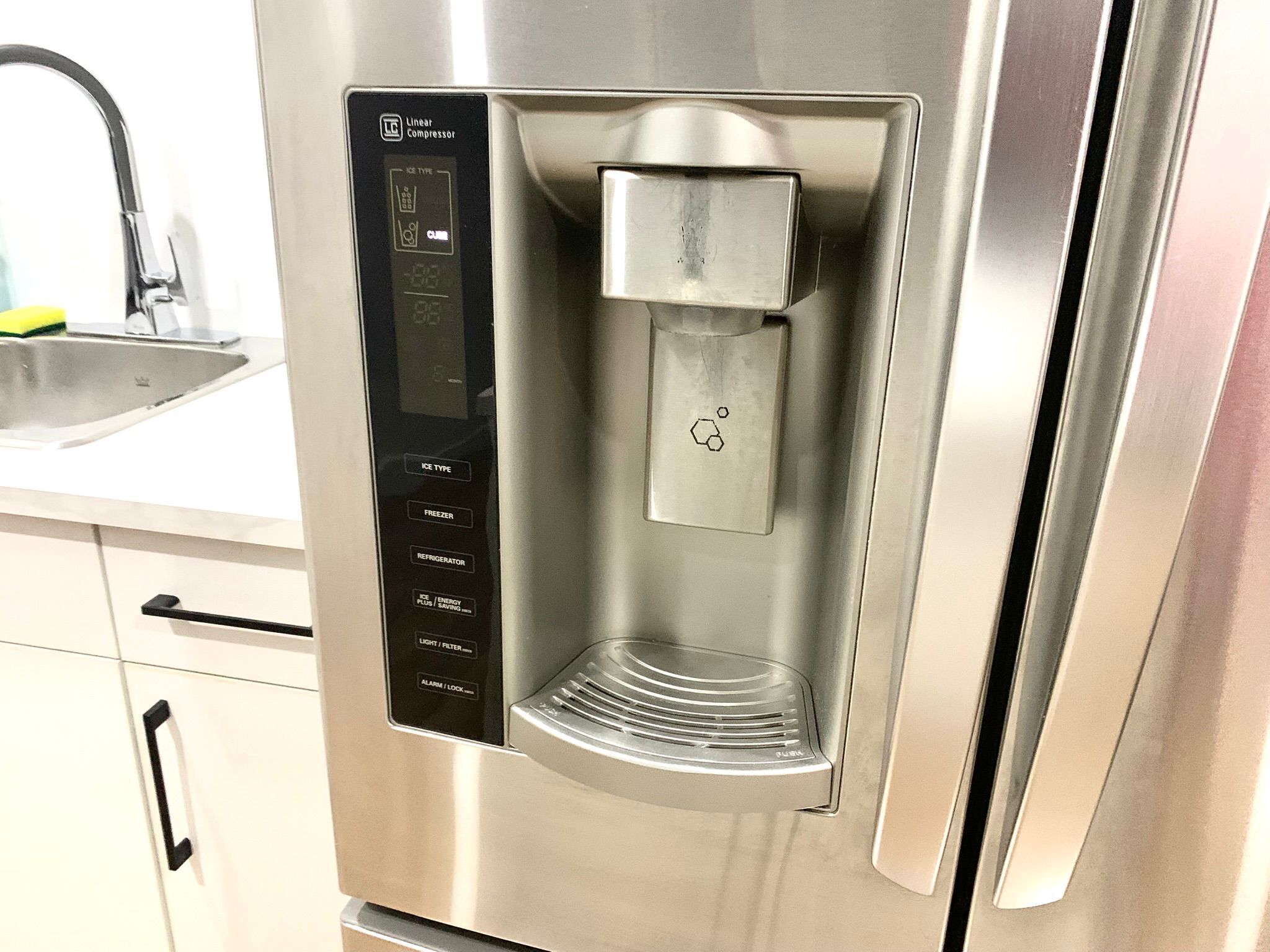 A stainless steel refrigerator with a built-in water dispenser and a digital control panel.